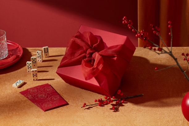 这张春节主题照片是从高角度近距离拍摄的。黄色桌子上放着一个红色礼品盒，周围展示着新年装饰配件。红色背景，留有设计空间。图片下载