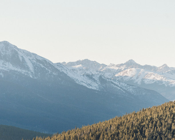 壮观的落基山脉雪山照片，前景是郁郁葱葱的山丘。图片下载