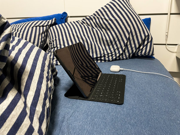 在舒适的床上，平板电脑、键盘和耳机的居家办公设置库存照片图片下载