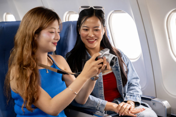 两个快乐的亚洲女孩一起旅行。她们在飞行中愉快地聊天，并查看相机中的照片。图片下载