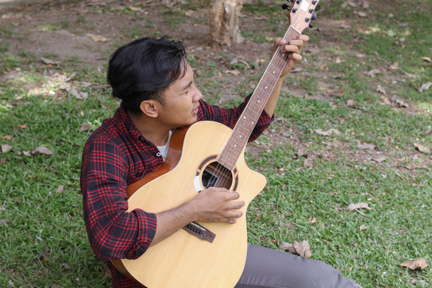 早晨在城市公园里弹吉他的迷人亚洲男子的户外照片图片下载