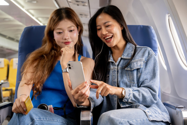 两个快乐的亚洲女孩一起旅行。她们在飞行中愉快地聊天，并查看相机中的照片。图片下载