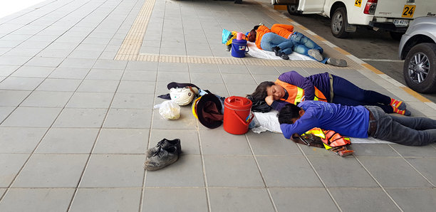 在泰国曼谷，午餐后人们或工人在人行道上睡觉，身旁有安全头盔、鞋子和汽车背景。这是一张街头生活的照片。图片下载