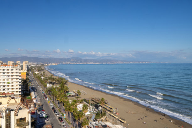 西班牙托雷莫利诺斯镇海滩的航拍照片，展示了阳光明媚的日子里海滩和海洋，以及海滩上的酒店和公寓。图片下载