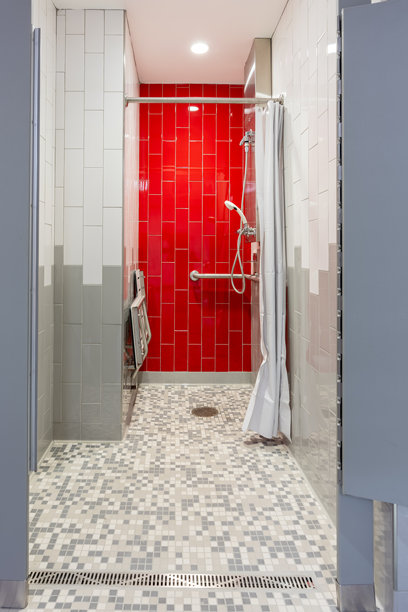 新单人私人健身房更衣室淋浴的竖直照片，红色瓷砖墙、长椅、瓷砖地板和白色淋浴帘。图片下载