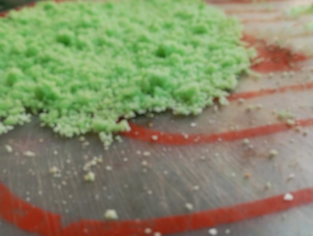 模糊的照片，展示了散落在平面上的鲜艳绿色蛋糕屑，可能是为装饰或烹饪用途而准备的。图片下载