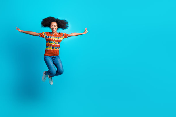 一只疯狂飞翔的鸟与一位年轻时尚女孩（卷发，穿着休闲牛仔裤和条纹T恤）在蓝色背景下的照片图片下载