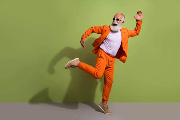 穿着橙色西装的搞笑表演者在绿色背景下的空旷空间中跳舞的全身照片图片下载