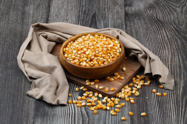 未爆开的爆米花在木碗中，背景为木质表面。这是一种玉米，受热后会从种子膨胀并鼓起。黄色的种子，适合食用，生食和素食。孤立的微距特写照片。图片下载