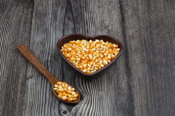 未爆开的爆米花放在木碗中，背景为木质表面。这是一种玉米，受热后会从种子膨胀并鼓起。黄色的种子，可食用，生食和素食食品。孤立的微距特写照片。图片下载
