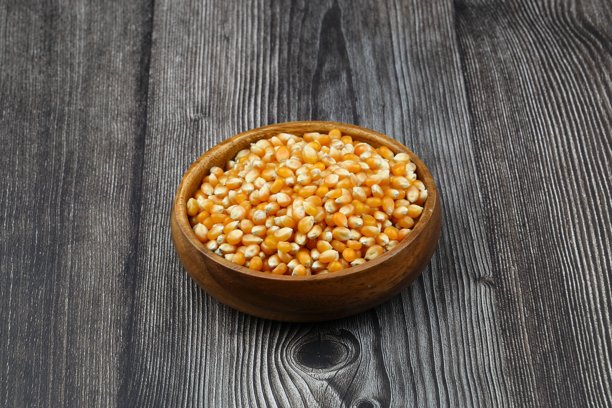 未爆开的爆米花在木碗中，背景为木质表面。这是一种玉米，受热后会从种子膨胀并鼓起。黄色的种子，适合食用，生食和素食。孤立的微距特写照片。图片下载