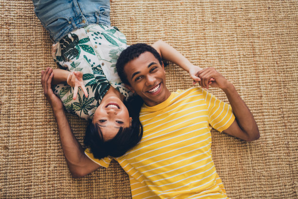 俯视照片显示一对可爱甜蜜的快乐夫妻穿着T恤，躺在地毯上享受室内浪漫约会。图片下载