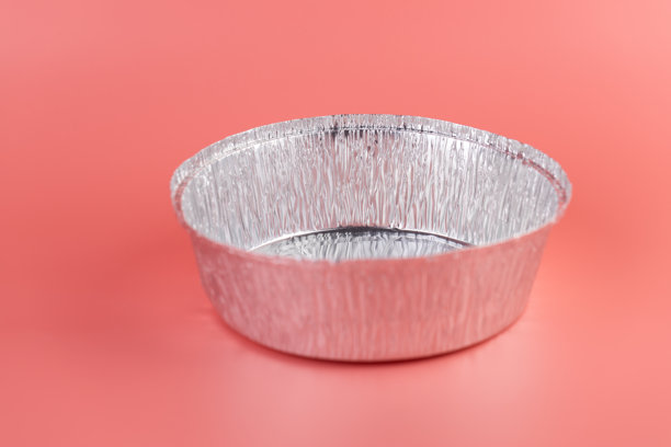 在柔和的粉色背景上，摆放着新的厨房铝箔圆形烘焙模具，现代科技带来厨房的清洁与实用，防洪系统设计。图片下载