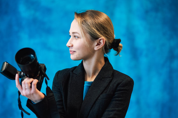 女性摄影师在摄影棚中的照片。她手持数码相机，背景为蓝色。图片下载
