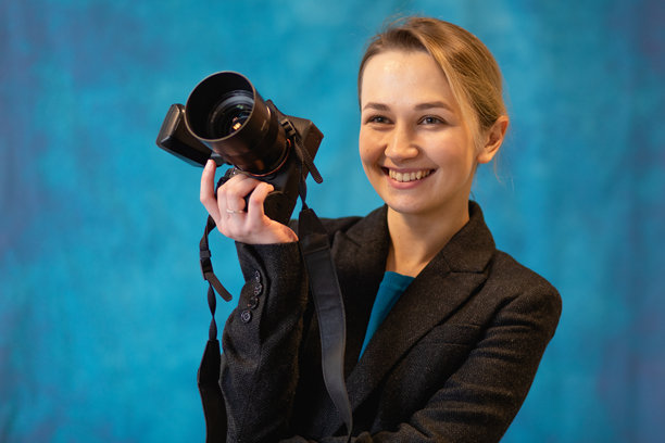 女性摄影师在摄影棚中的照片。她手持数码相机，背景为蓝色。图片下载