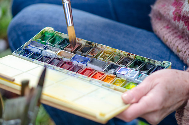 冬季户外，一位年长女性正在绘制水彩画，捕捉着风景中宁静的美丽和雪花的点缀 - 特写她手中握着水彩调色板的画面 - 股票照片图片下载