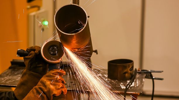 一名戴着防护面具的焊工正在切割金属管道。竖版照片。图片下载