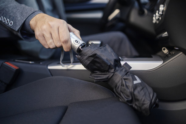 在雨天，一位穿着休闲商务装的男士在车内拿着雨伞的裁剪照片。图片下载