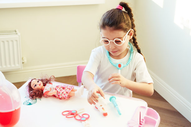 可爱的幼儿女孩穿着白色外套，手持注射器，正在给她的洋娃娃扮演医生并提供医疗护理。儿童角色游戏。新冠疫苗接种概念。高质量照片图片下载