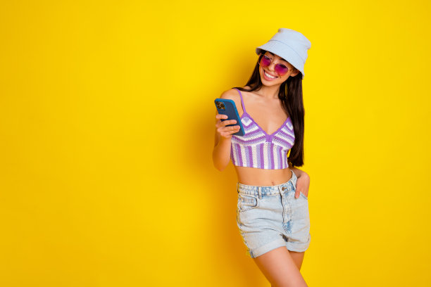 迷人的年轻社交媒体影响者在黄色背景下冲浪，使用智能手机与朋友聊天的照片图片下载