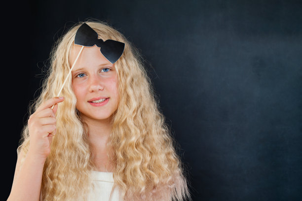 微笑的年轻女孩在黑色背景下摆姿势，手持照片亭道具和蝴蝶结图片下载