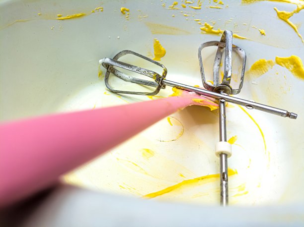 一个特写镜头，展示了一个混合碗，里面有黄色面糊的残留物和两个金属打蛋器，其中一个有粉色手柄，适用于烘焙。这张图片捕捉了烘焙后的场景。图片下载