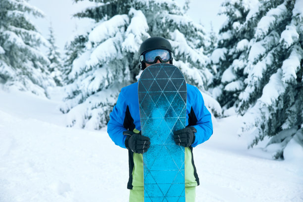 滑雪胜地的男子滑雪者，背景是蓝天，手持滑雪板。佩戴滑雪眼镜，眼镜上反射着被雪覆盖的山脉。图片下载