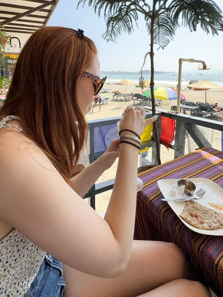 迷人的特写照片，红头发的女人穿着休闲的夏装，短裤，露肩上衣和太阳镜，坐在海滩小屋的阳台上吃早餐，马萨拉薄饼和酸辣酱，重点放在前景图片下载