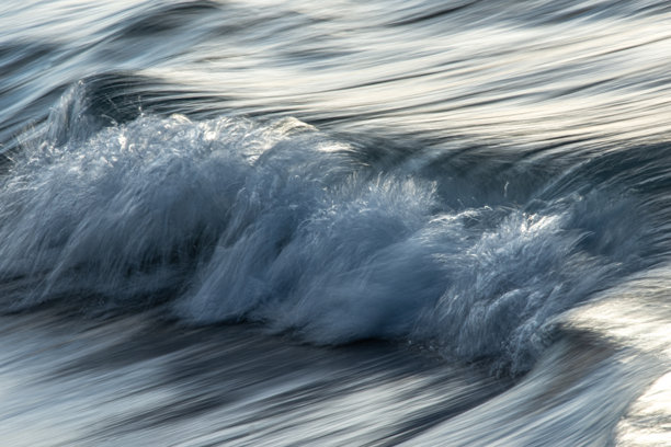 长时间曝光的海浪照片，展现出模糊的运动。水面反射着日落时分天空的色彩。图片下载