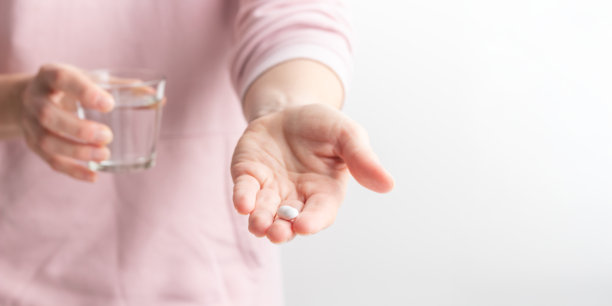女性在白色背景下服用药物，手中握着白色药丸和一杯水。健康护理、膳食补充剂、抑郁症和疾病治疗的概念。高质量的照片横幅。图片下载