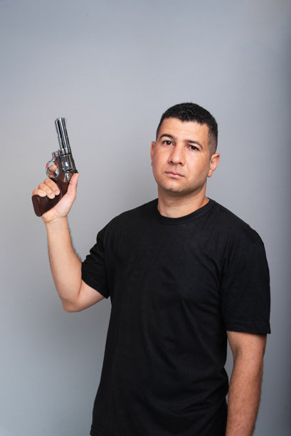 一位英俊的男子穿着黑色衬衫和牛仔裤，手持枪支，直视镜头。图片下载