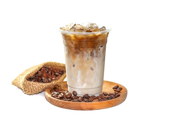 冰拿铁咖啡盛在塑料杯中，放在木盘上，咖啡豆散落在白色背景上，呈现孤立的照片风格。图片下载