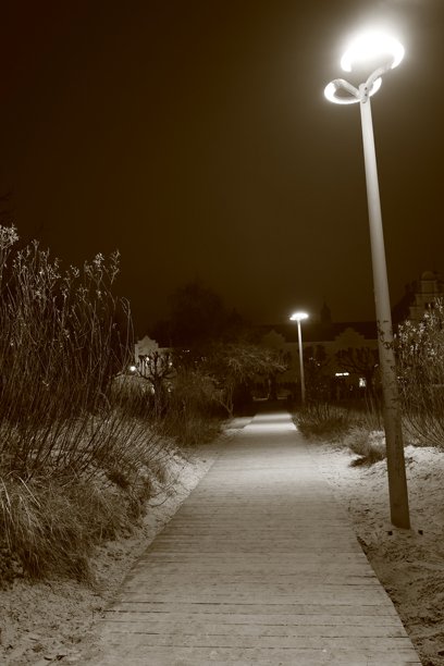 夜晚的木栈道通往沙滩，周围是沙子，街灯照亮，黑白照片图片下载