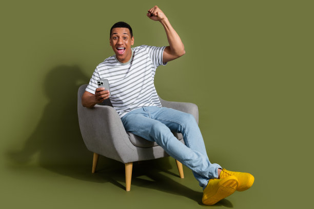 全身照片，幸运的好心情男孩穿着条纹T恤，赢得游戏，现代设备，空旷空间，孤立的卡其色背景。图片下载