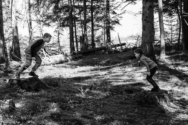 两个孩子在树林中的树桩上顽皮地跳跃。黑白照片捕捉了童年的乐趣和冒险。图片下载