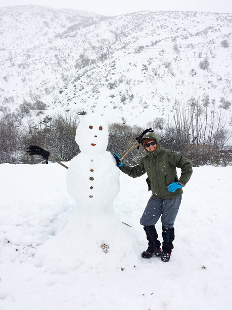 女人在雪人旁微笑，雪景如画。竖版照片图片下载