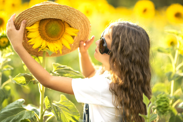 可爱的女孩戴着草帽，眼镜上有向日葵，站在向日葵田里。搞笑而快乐的夏季儿童照片。图片下载