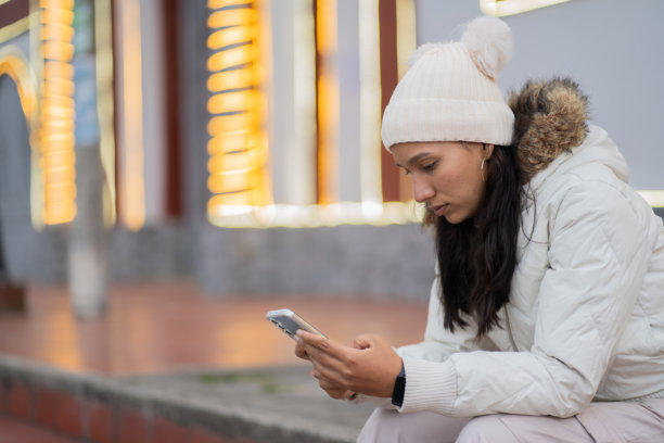 年轻女性坐在楼梯上，使用手机打字并查看社交媒体消息 - 股票照片图片下载