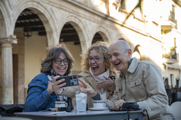 三位老朋友在户外咖啡馆分享照片，欢笑并享受愉快的时光图片下载