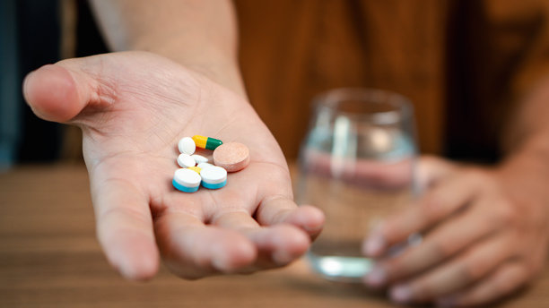 男性手握着膳食补充剂，维生素C、B、鱼油，并握着一杯水，手掌上的膳食补充剂或药丸特写照片图片下载
