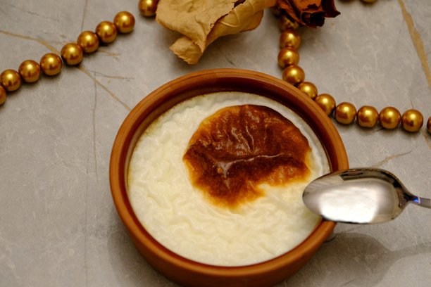 烤米布丁的特写照片，放在砂锅中，旁边有一把金属勺子，背景为灰色。图片下载