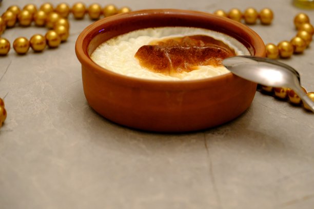 烤米布丁的特写照片，放在砂锅中，旁边有一把金属勺子，背景为灰色。图片下载