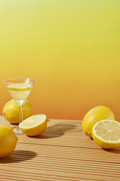 渐变的黄色背景与一些新鲜的柠檬和一个鸡尾酒杯柠檬汁特色的木制桌子。前视图照片与空白的空间表示图片下载