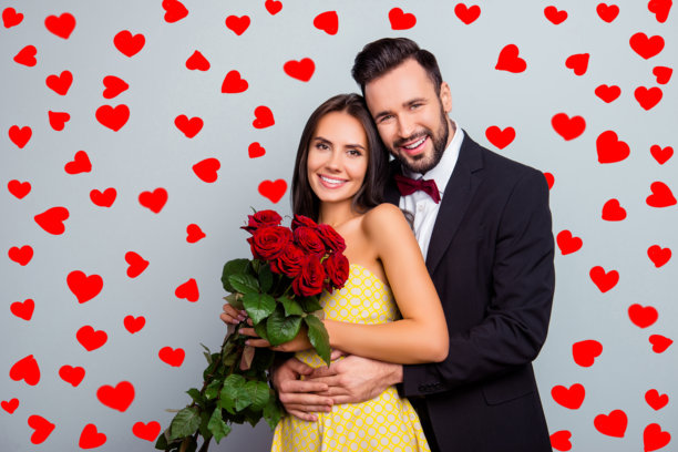 一对穿着优雅的年轻夫妻的肖像照片，面带微笑，迷人可爱，女人手中捧着一束红玫瑰，准备庆祝生日派对，背景为灰色。图片下载