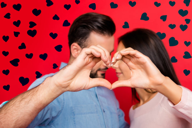 他和她之间爱的概念照片。吸引人的可爱情侣在红色背景前，鼻尖相触，手指交叉形成心形的特写肖像，庆祝3月8日。图片下载