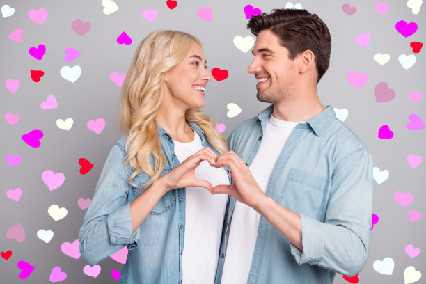 年轻情侣的侧面照片，快乐积极，微笑着用手指做出心形符号，表达爱意，背景为灰色。图片下载