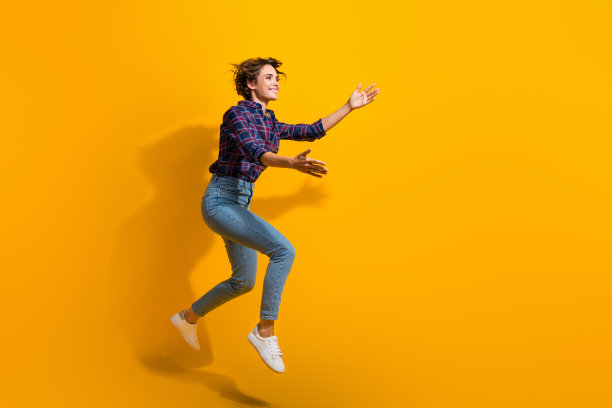 穿着格子衬衫和牛仔裤的可爱女性在黄色背景上从空中抓取产品的全身照片图片下载