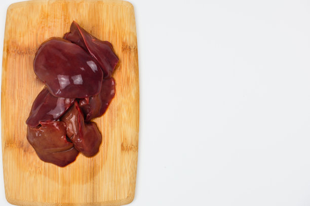 顶部视角，垂直特写照片，鸡肝位于木砧板中央，背景为白色，留有文本空间。健康营养、维生素和微量元素对身体的重要性，有机食品的概念。图片下载