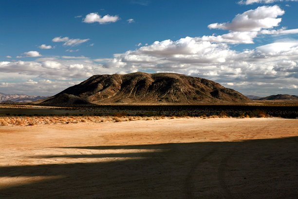 美丽的沙漠风景照片，背景是一座山，天空中布满了白云，呈现出戏剧性的蓝色。图片下载