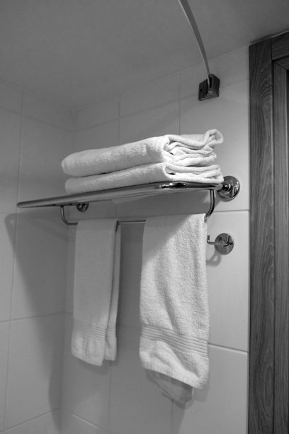 一张黑白照片，展示了酒店房间白色浴室内金属挂架上的白色毛巾。图片下载